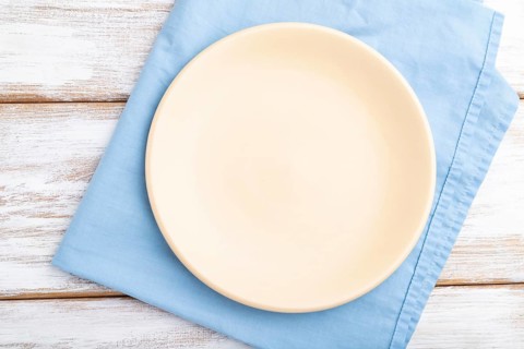 Empty ceramic plate on white wooden background and blue linen textile. Top view, close up, flat lay