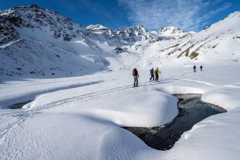 Small stream in a snow-covered mountain landscape, ski tourers in a valley, ascent to the