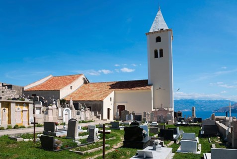 Old church with cemetery and bell tower against a mountain backdrop under a blue sky, Church of St