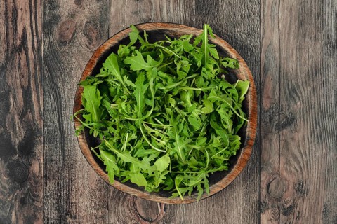 A rustic wooden bowl with fresh arugula leaves on a textured wooden table, showcasing vibrant