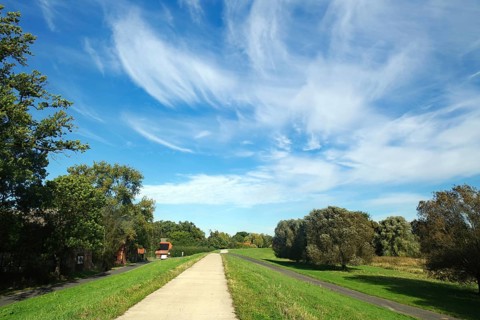 Long path on a dyke under a picturesque sky with clouds and surrounded by green landscape, cycle