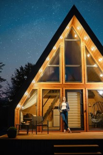 Dreamy woman stands on the doorway of a large wooden cabin late at night