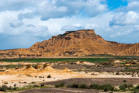 Majestic mountain in a dry desert landscape, partly cloudy with scattered green vegetation against