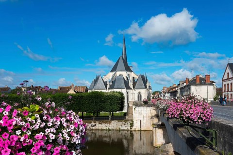 Ansicht einer Kirche in einem kleinen Dorf mit blauen Himmel und weißen Wolken, umgeben von Blumen