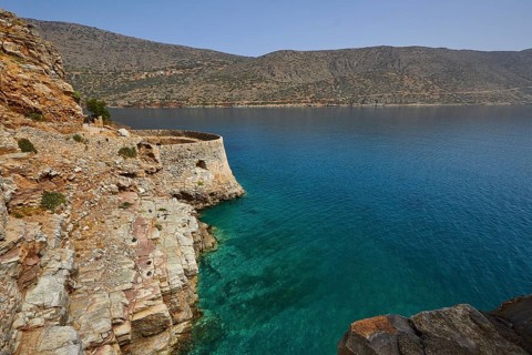 Rustic stone wall on cliffs above a turquoise sea with mountains in the distance, Venetian sea