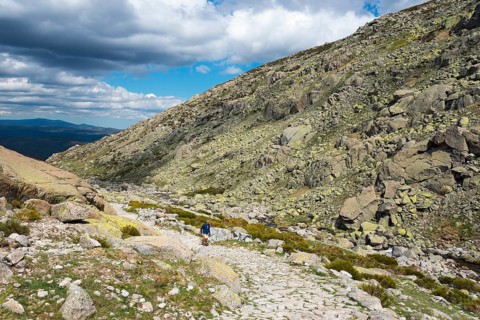 A hiking person on a stony path through a rocky mountain landscape under a cloudy sky, Hiking area,