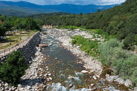 Landschaft mit einem gebirgigen Fluss, der durch eine grüne und steinige Landschaft fließt, umgeben
