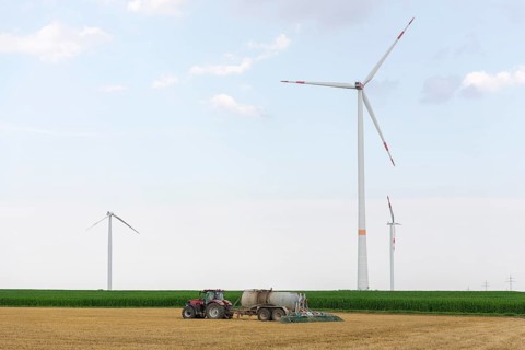 Farmer spreading liquid manure on a harvested grain field, wind farm, defective wind turbine with a