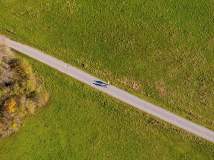 Green meadow with a narrow road and a person casting shadows on the road, high ropes course,