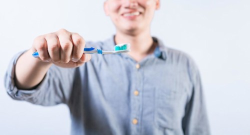 Smiling person showing toothbrush with toothpaste isolated. Unrecognizable man holding brush with