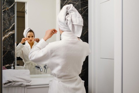Woman wrapped her hair in towel after shower looking in mirror and fixing towel