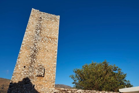 Standing old tower made of pebbles under a bright blue sky, Flomochori, residential towers village,