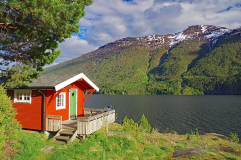 Red-painted cabin on the shore of a fjord against a backdrop of mountains and forest, holiday