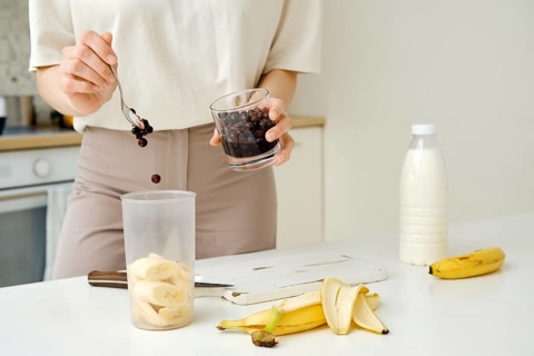 Unrecognizable woman puts blackcurrants in a blender to mix them with a chopped banana