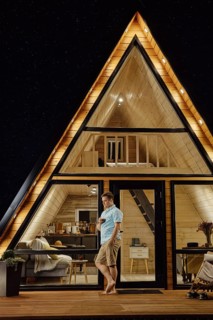Man with a glass in his hand standing on terrace of tiny house at late evening and enjoys calmness