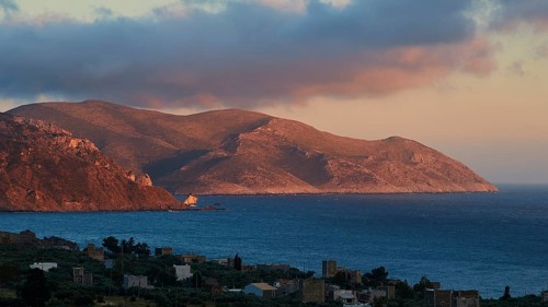 A mountain landscape at dusk with a view of the sea and a small settlement in the foreground, Mani