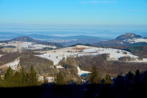 Snow-covered hilly landscape under a blue sky with trees in the foreground, Milseburg,