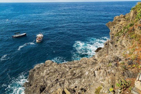 Rocky cliff and fishing boats moored in bay, Ligurian Sea, Manarola village in late summer, Cinque