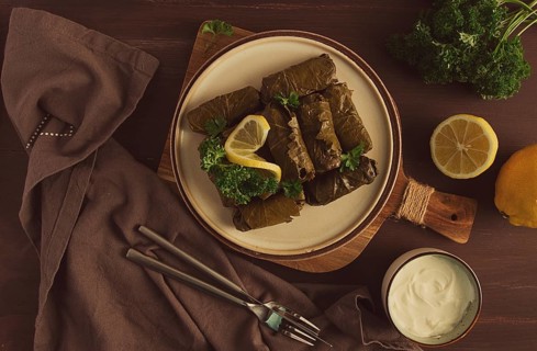 Dolma, cabbage rolls, grape leaves with filling, white sauce, lemon and herbs, rustic, selective