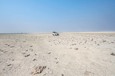 Four-wheel drive Toyota Hilux with roof tent, driving over salt pan, lone car in large wide plain,