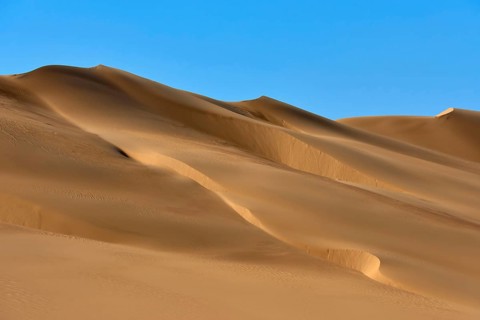 Sand dunes under a blue sky, conveying a calm and vast desert landscape, Matruh, Great Sand Sea,