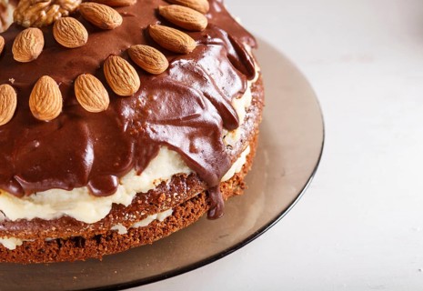 Homemade chocolate cake with milk cream, caramel and almonds on white wooden background. close up