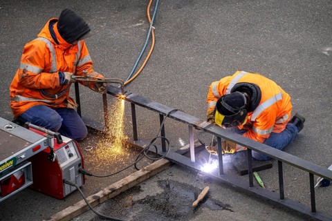 Locksmith at work, cutting and welding, on a workpiece in an industrial plant, a metal ladder is