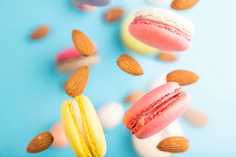 Multicolored flying macaroons and almonds eggs frozen in the air on blurred blue background. top