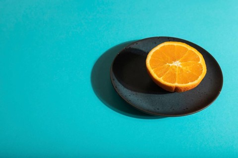 Ripe cut orange on blue ceramic plate on blue pastel background. Side view, copy space, hard light.