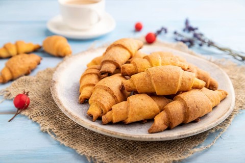 Homemade bagel roll with cup of coffee on a blue wooden background and linen textile. side view,
