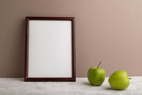 Brown wooden frame mockup with green apple on beige paper background. Blank, vertical orientation,
