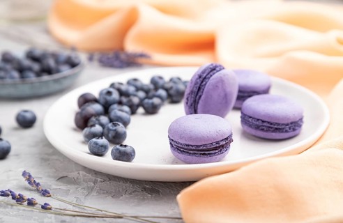 Purple macarons or macaroons cakes with blueberries on white ceramic plate on a gray concrete