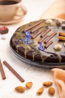 Homemade chocolate brownie cake with caramel cream and almonds with cup of coffee on a white