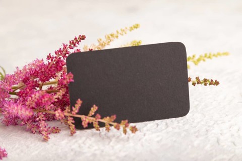 Black paper business card mockup with purple astilbe flowers on gray concrete background. Blank,