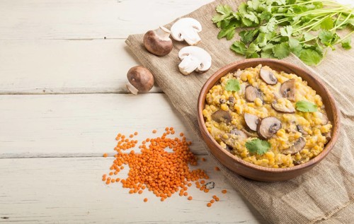 Lentils porridge with champignons and coriander in a wooden bowl on a white wooden background and