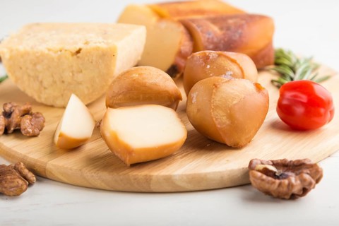 Smoked cheese and various types of cheese with rosemary and tomatoes on wooden board on a white