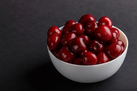 Fresh red sweet cherry in white bowl on black background. side view, close up