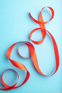 Red coral ribbon on a blue pastel background. Celebration concept. Top view, close up, flat lay