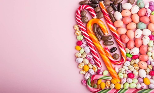 Colorful multicolored candies on a pink pastel background. Christmas cane, chocolate eggs, caramel