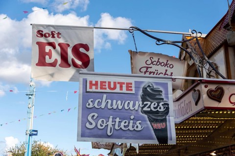 Advertising sign for black soft ice cream on a fairground with blue sky in the background,