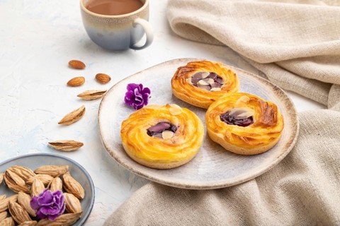Small cheesecakes with jam and almonds with cup of coffee on a white concrete background and linen