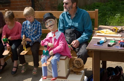 Man and children operating a traditional wooden jig doll dancer during a country folk event at