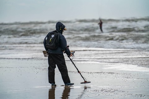 Treasure hunter, man with metal detector on the beach, dark storm clouds, autumn at the North Sea