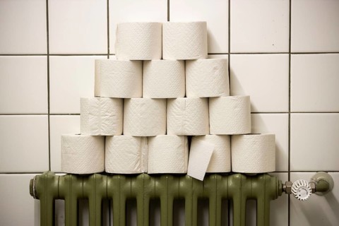 Toilet paper rolls stacked on a radiator in a public toilet