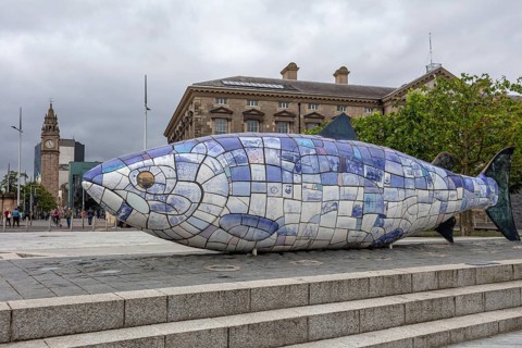 Colourful fish sculpture made of tiles in a public square in front of a historic building, Belfast