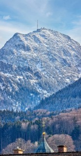 Snow-covered mountain with a church in the foreground under a clear blue sky, Bad Feilnbach