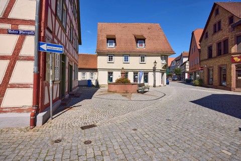 Running fountain with half-timbered house and historical buildings under a cloudless blue sky on