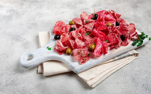 Assorted, meat appetizer, prosciutto, salami and ham, with olives, on a wooden white board, light