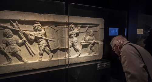 Visitor looking at tomb relief fragment showing gladiators fighting in ancient Rome in the
