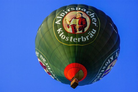 A hot air balloon with advertising for Alpirsbacher Klosterbräu takes to the air with passengers on